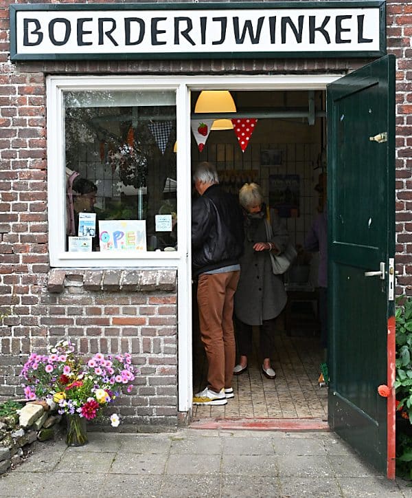 De deur van de boerderijwinkel van biologisch- dynamisch landbouwbedrijf De Zonnegaard in Voorst, staat open en er zijn een aantal klanten binnen. Bij de ingang staat een mooie bos bloemen van de pluktuin.