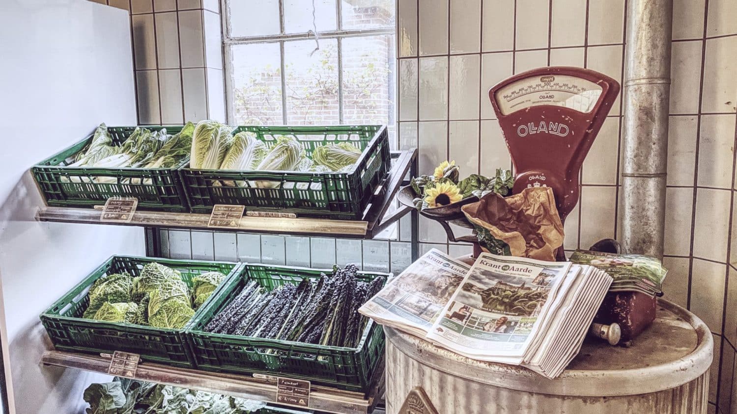 Sfeerbeeld in sepia-tonen van de boerderijwinkel van biologisch- dynamisch landbouwbedrijf De Zonnegaard in Voorst, met o.a. een ouderwetse weegschaal en de gratis mee te nemen ‘Krant van de Aarde’.