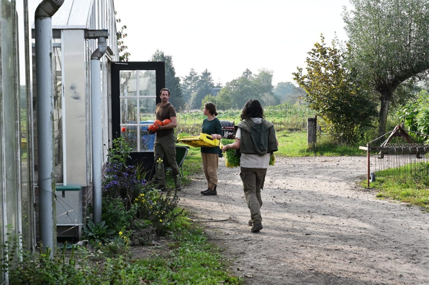 De medewerkers van De Zonnegaard zijn kort in overleg bij de open deur van de kas, met pompoenen en andere biologisch dynamische groenten in hun handen.