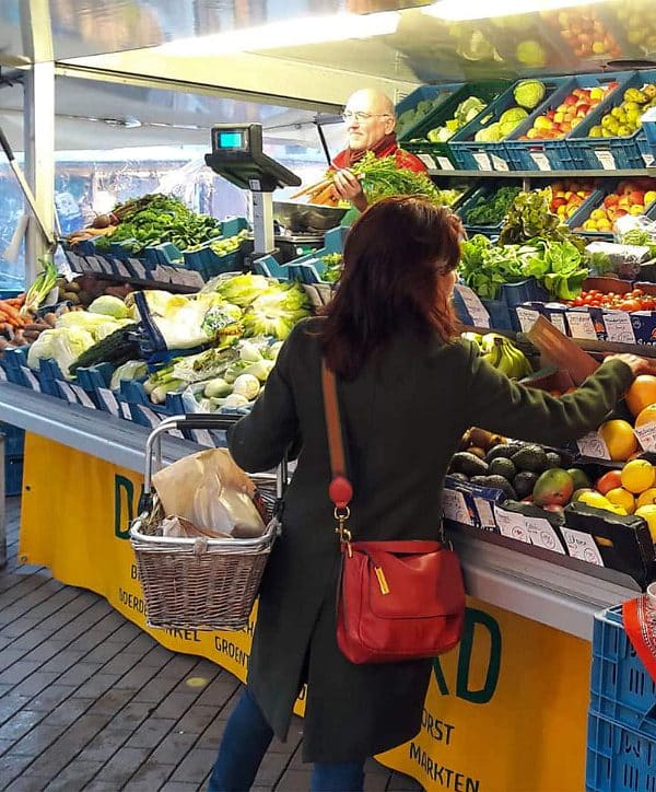Een klant met een rieten boodschappenmand aan haar arm, kiest bij de marktkraam van De Zonnegaard in Deventer of Zutphen, haar biologisch dynamisch geteelde groenten en fruit uit.